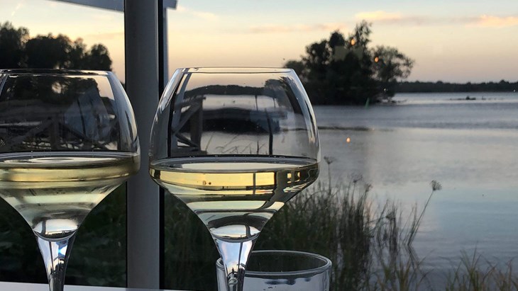Två vinglas med vitt vin och en solnedgång över sjön.
